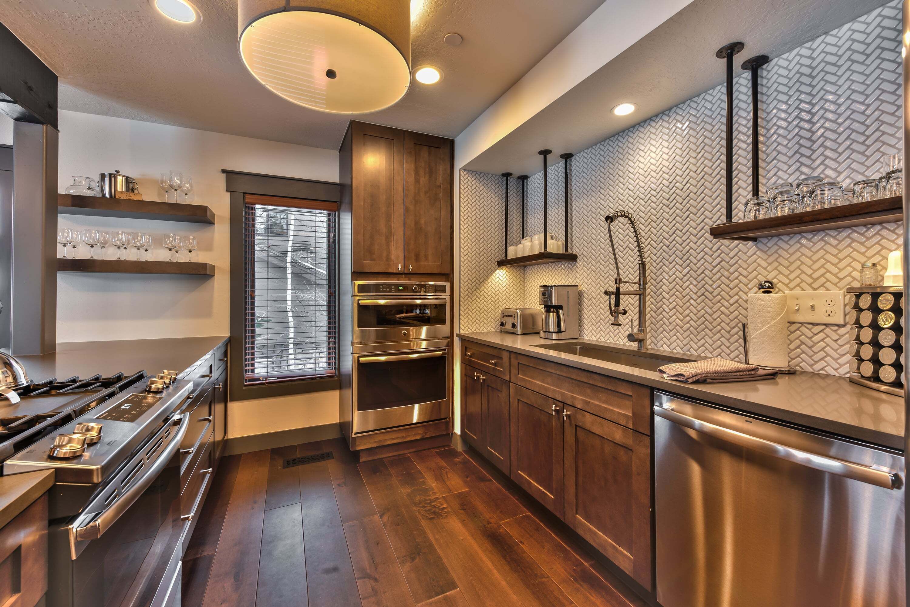 A modern kitchen with stainless steel appliances, wooden cabinets, and a herringbone-patterned backsplash.