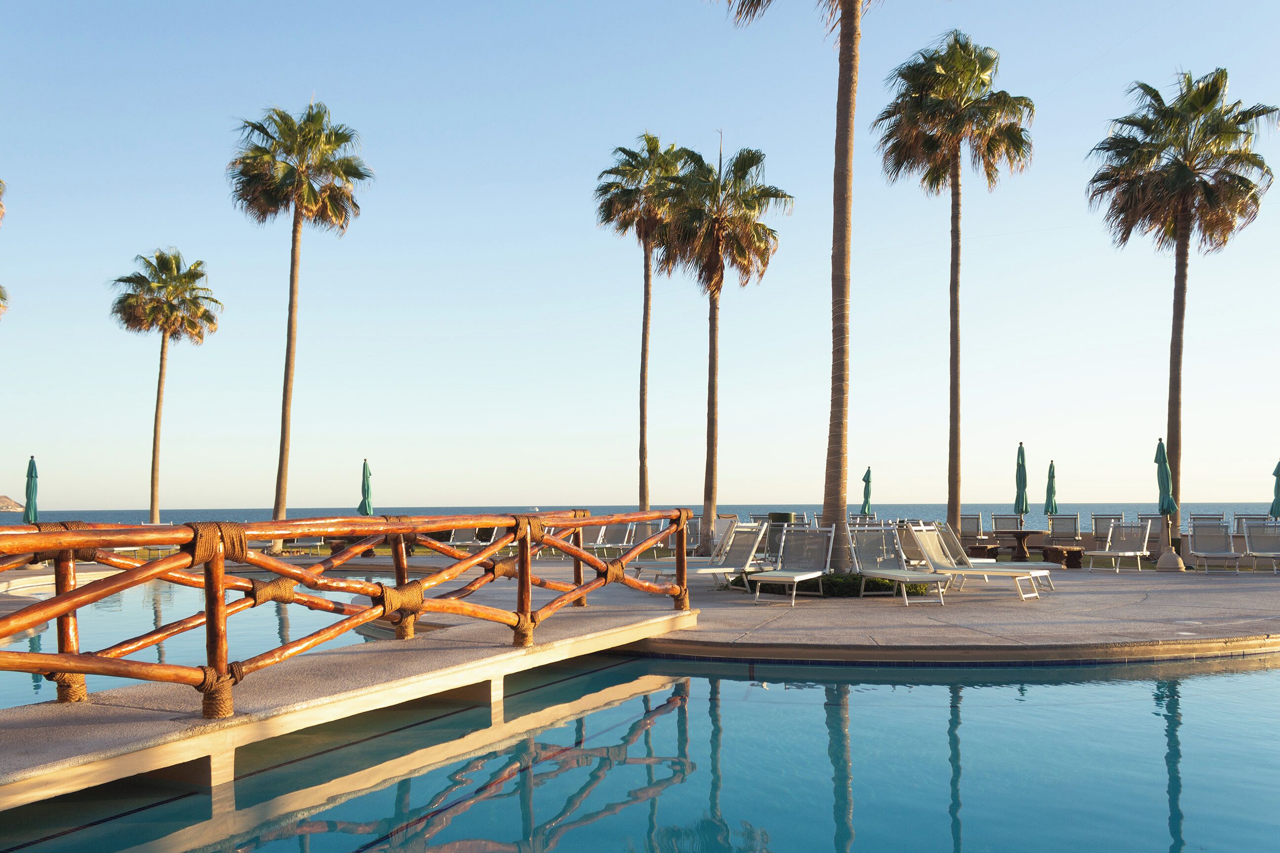 A poolside area with lounge chairs and palm trees, overlooking a body of water.