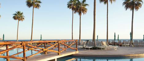 A poolside area with lounge chairs and palm trees, overlooking a body of water.