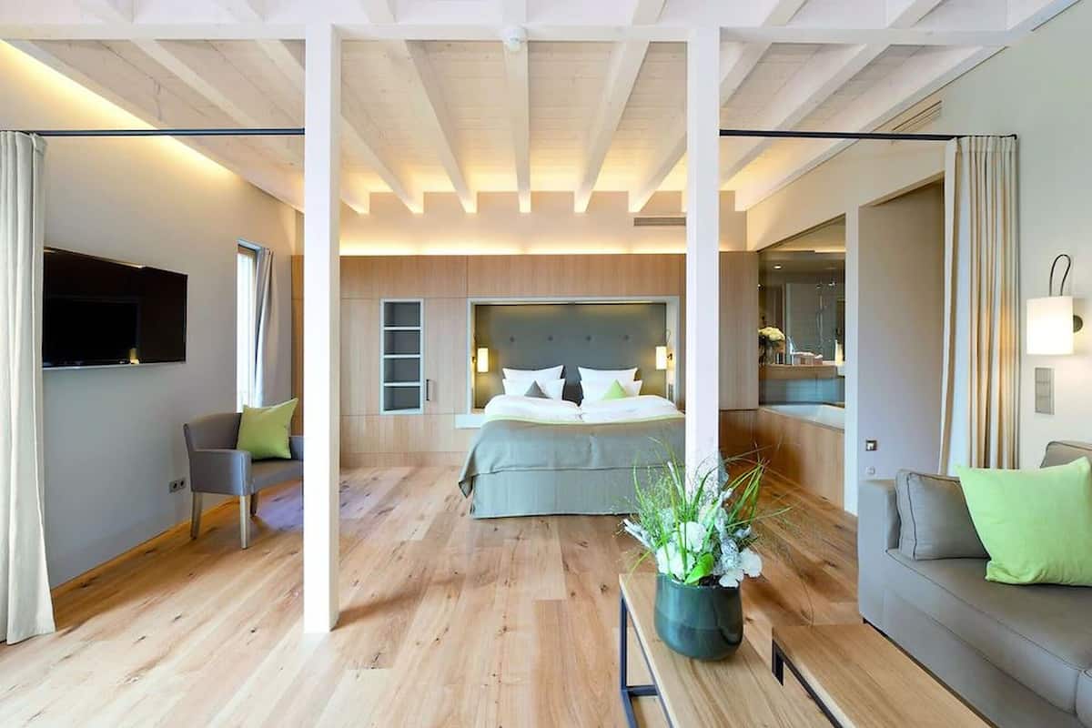 Une chambre d’hôtel moderne dotée d’un grand lit, d’un téléviseur à écran plat, d’un coin salon avec un canapé et un fauteuil, ainsi que d’un coin repas avec une table et des chaises.
