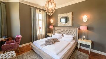 Un dormitorio con una cama grande, cabecera capitonada, dos mesitas de noche con lámparas, un espejo en la pared y una silla.