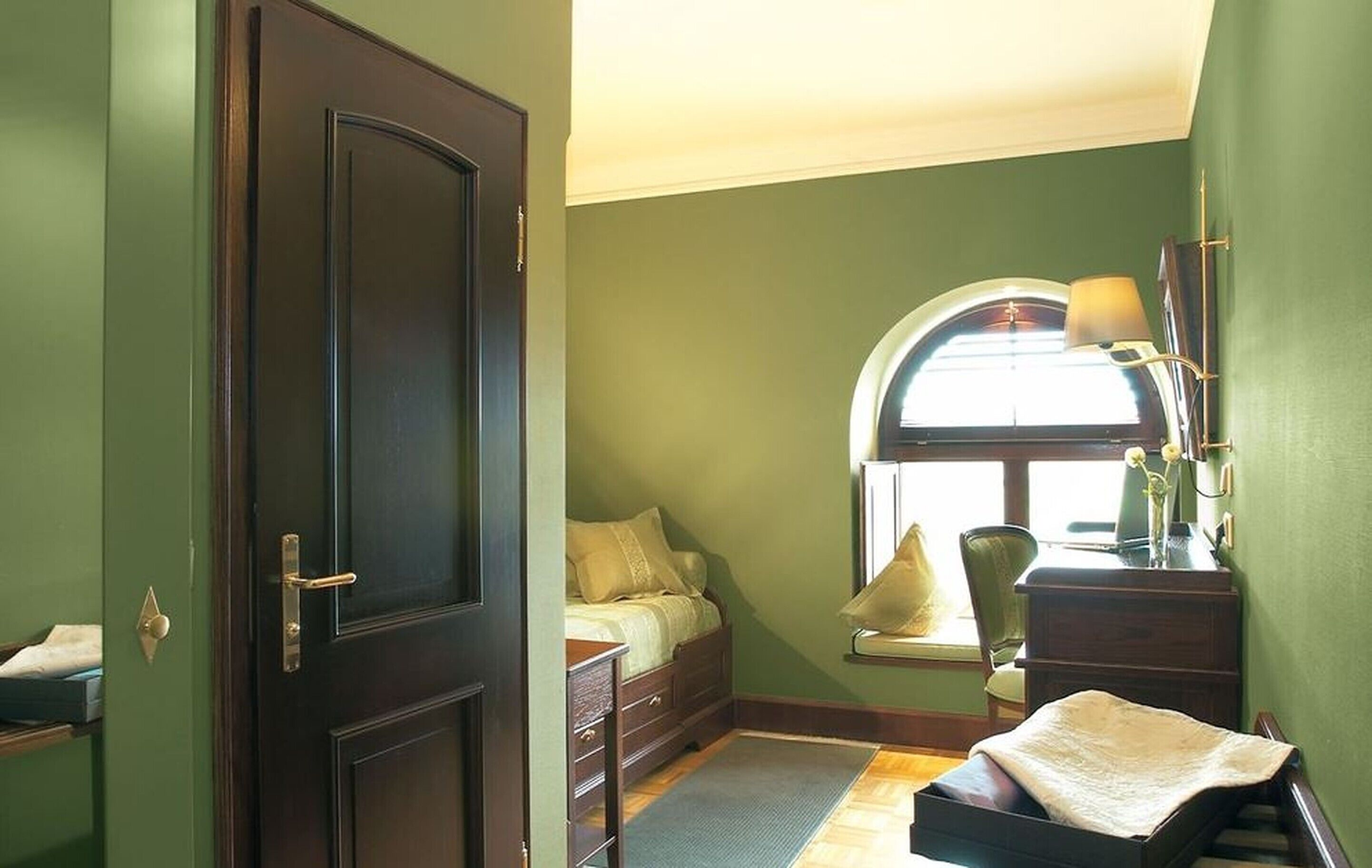 A bedroom with a bed, a desk, a chair, and a window with a lamp.