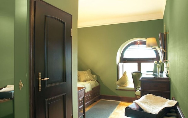 A bedroom with a bed, a desk, a chair, and a window with a lamp.