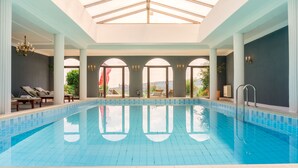 An indoor swimming pool with clear blue water, white tiled floor, and a skylight above.