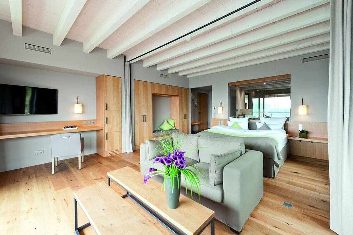 Une chambre d’hôtel moderne avec un bureau en bois, un canapé, un lit et une grande fenêtre.