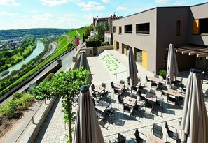 An outdoor terrace with tables and chairs, overlooking a river and greenery. - Schlosshotel Steinburg (Würzburg)