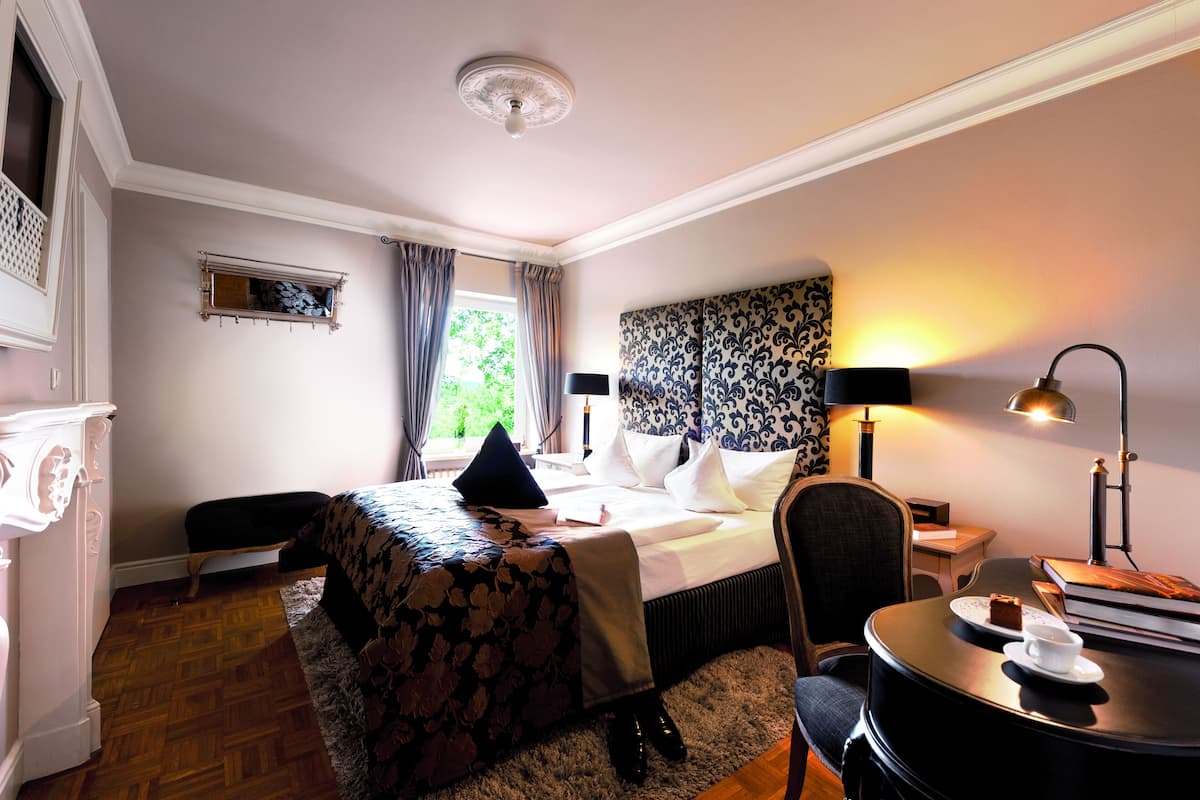 Une chambre d’hôtel équipée d’un lit, d’un bureau, d’une chaise, d’une lampe et offrant une vue sur la verdure environnante.
