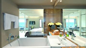 A modern bathroom with a large bathtub, a vanity with a mirror, and a view of a bedroom with a bed and a balcony.