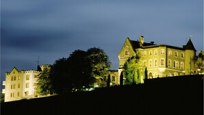 A historic building with multiple windows and a prominent tower, surrounded by trees.