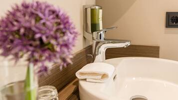 A bathroom sink with a white towel and a glass vase with purple flowers.
