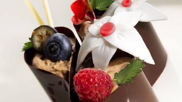 Un postre con chocolate, frutos rojos y detalles decorativos sobre un plato blanco.