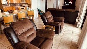 A living room with a brown leather sofa, a television, and a kitchen in the background.