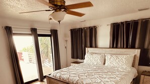 A bedroom with a bed, curtains, a ceiling fan, and a view of the outside.