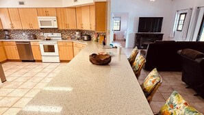 A modern kitchen with a central island, wooden cabinets, and a dining area with wicker chairs.