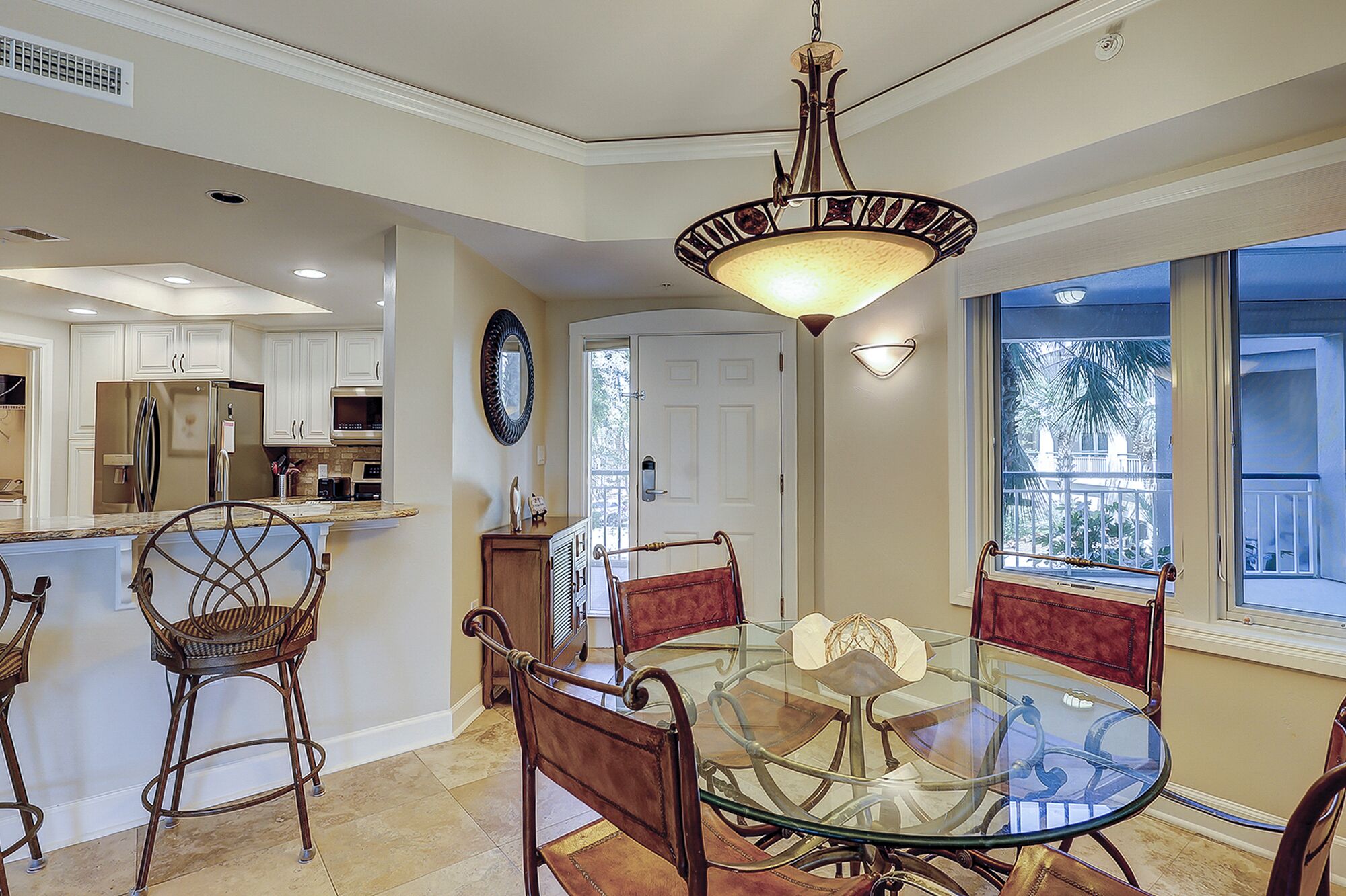 A dining area with a glass table and metal chairs, a kitchen with white cabinets, and a ceiling light fixture.
