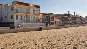 A beachfront property with a multi-story building, a balcony, and a sandy beach in the foreground.