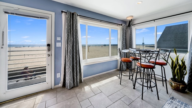 A room with a view of the beach, a table with chairs, and a potted plant.