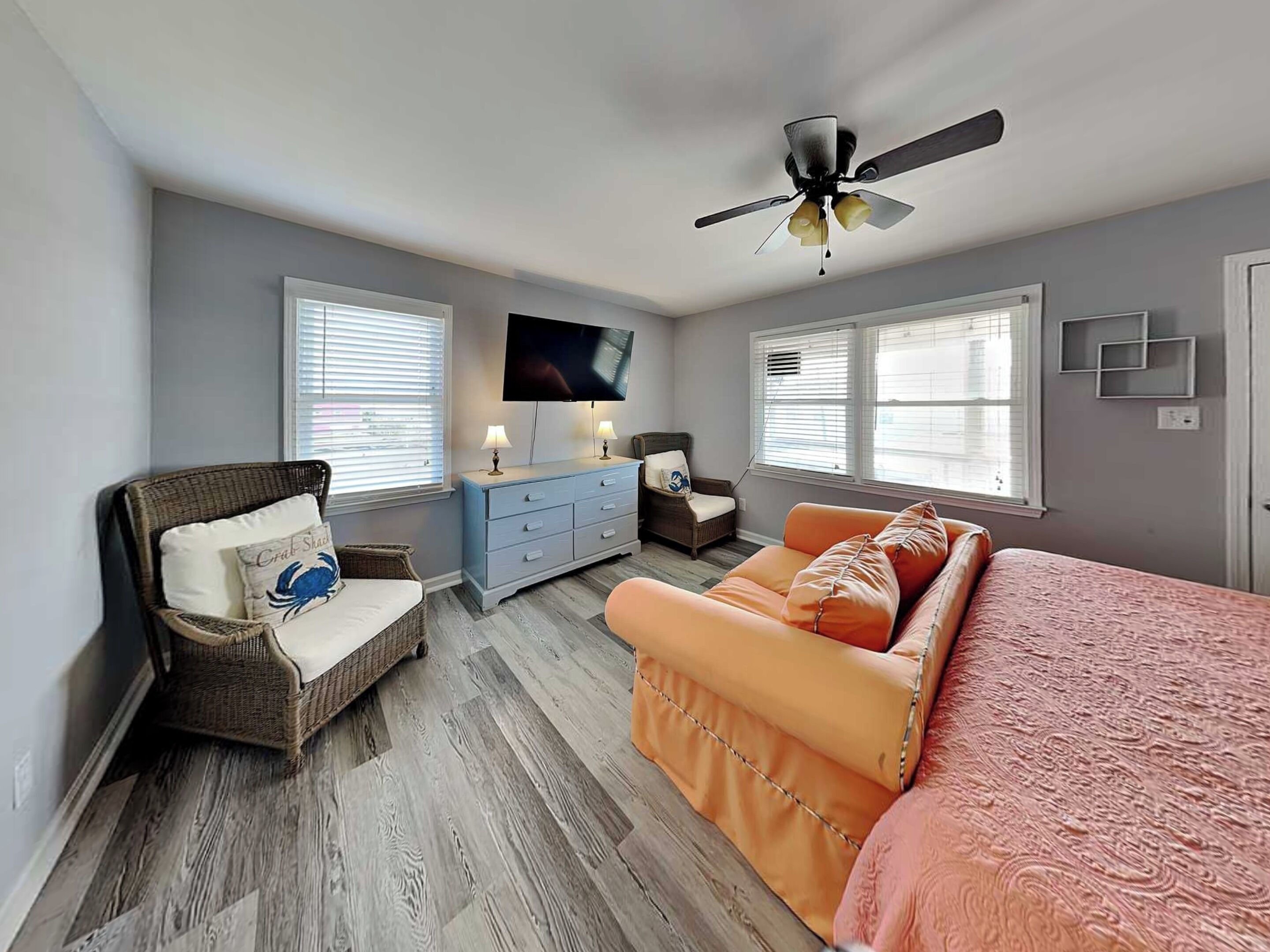 A bedroom with a bed, a chair, a dresser, a television, and a ceiling fan.