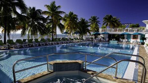 Zona de piscina con sillones de descanso y palmeras, rodeada por una valla blanca.