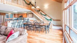 A spacious living area with a wooden staircase, a dining table with chairs, and a kitchen in the background. - V3 Gorgeous Ski-In slopeside Townhouse with Amazing Mountain Views in Bretton Woods. Dog Friendly! (Bretton Woods)