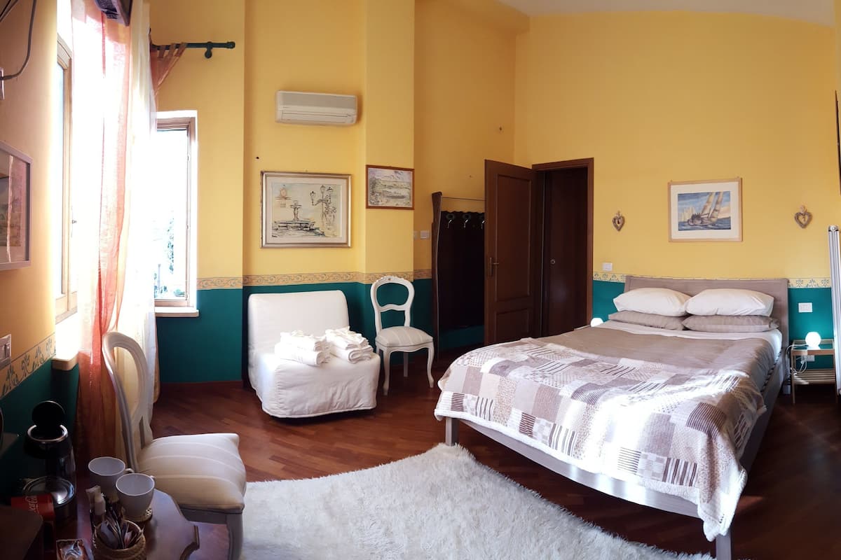Une chambre d’hôtel avec un lit, deux chaises, une petite table avec une machine à café et une fenêtre avec des rideaux.