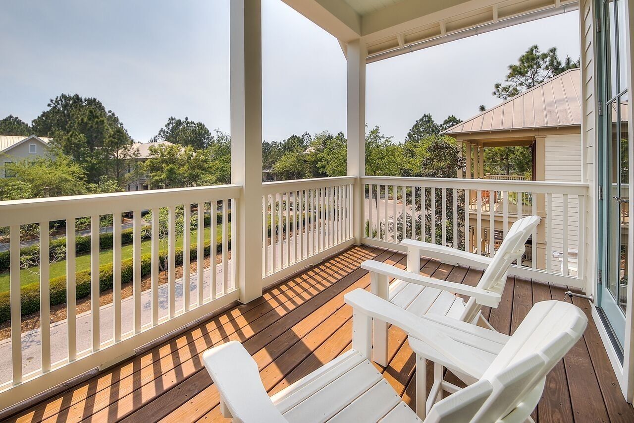 A covered porch with white chairs and a view of a residential street.