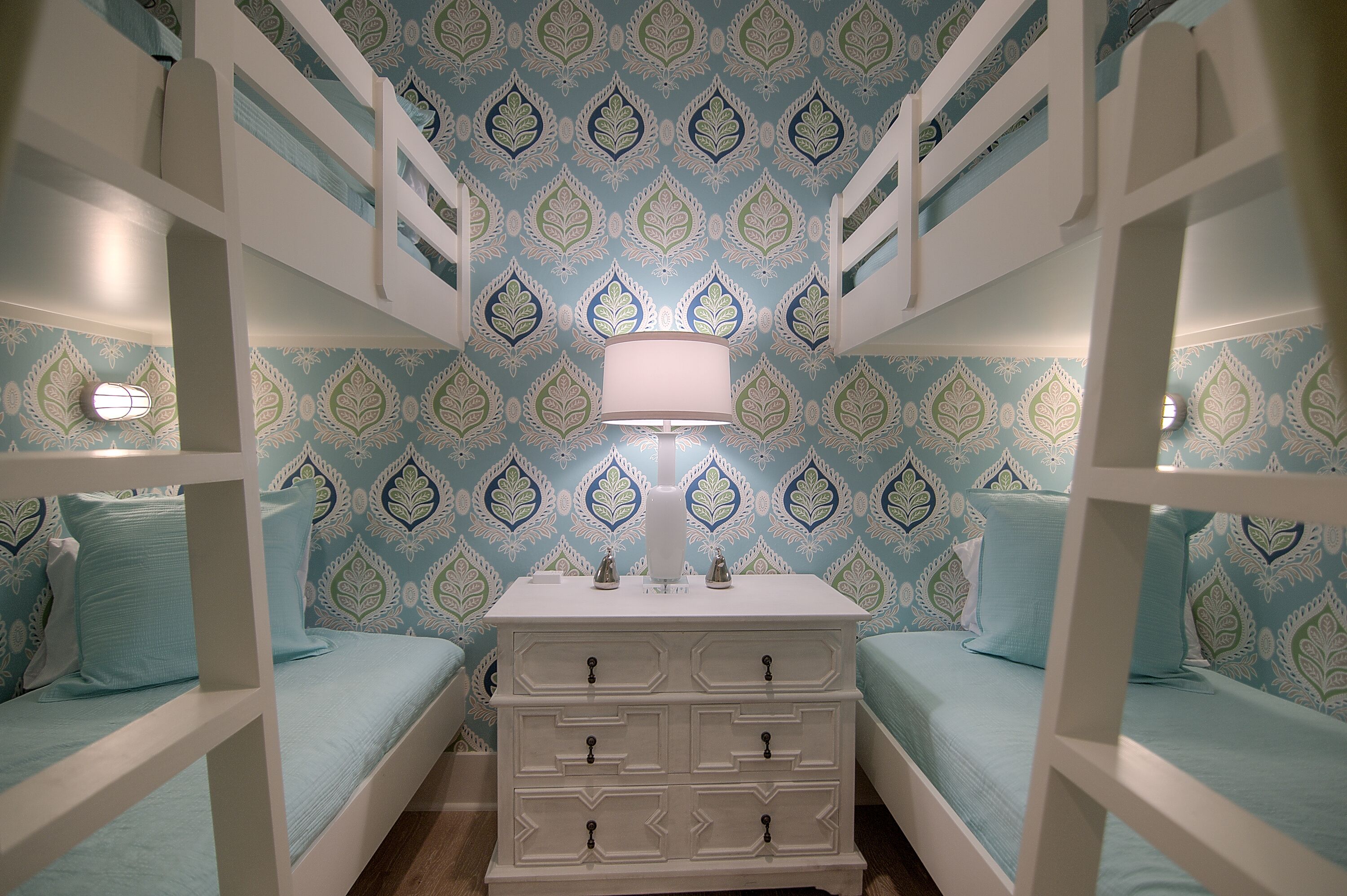 A room with bunk beds, a dresser, and patterned wallpaper.