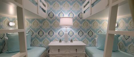 A room with bunk beds, a dresser, and patterned wallpaper.