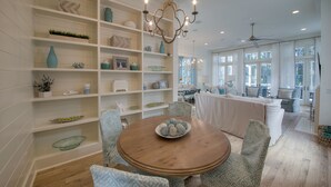 A dining area with a round wooden table, patterned chairs, and a decorative bowl. Shelves with various items line the walls. - Last minute discount July 5-11!  Watercolor Camp district 5BR w/ Pool & Spa (Santa Rosa Beach)