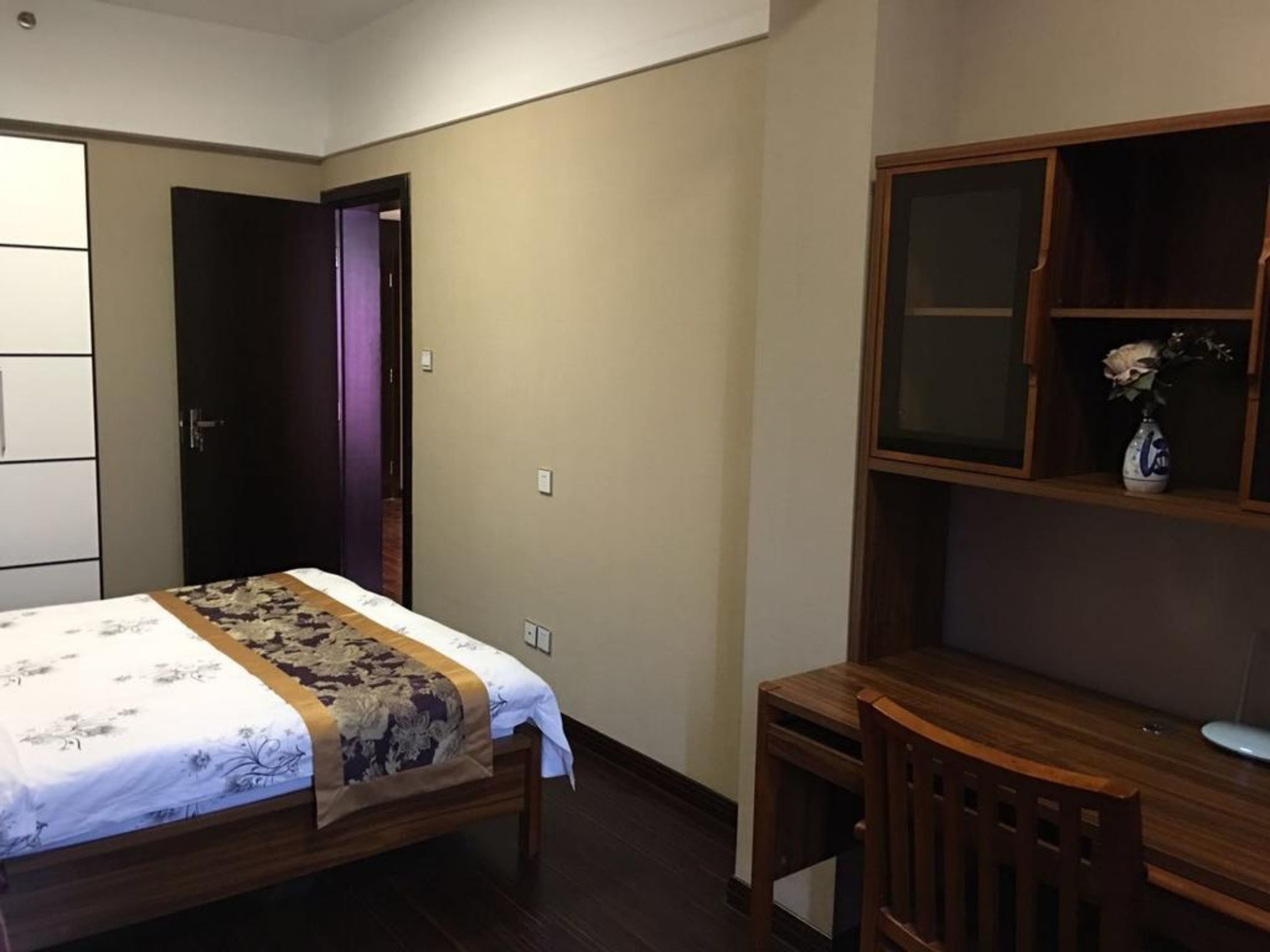 A bedroom with a bed, a wooden desk, and a cabinet.