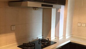 A modern kitchen with dark cabinetry, a black stovetop, and white tiled walls. - Zixinju Aparthotel (Changsha)