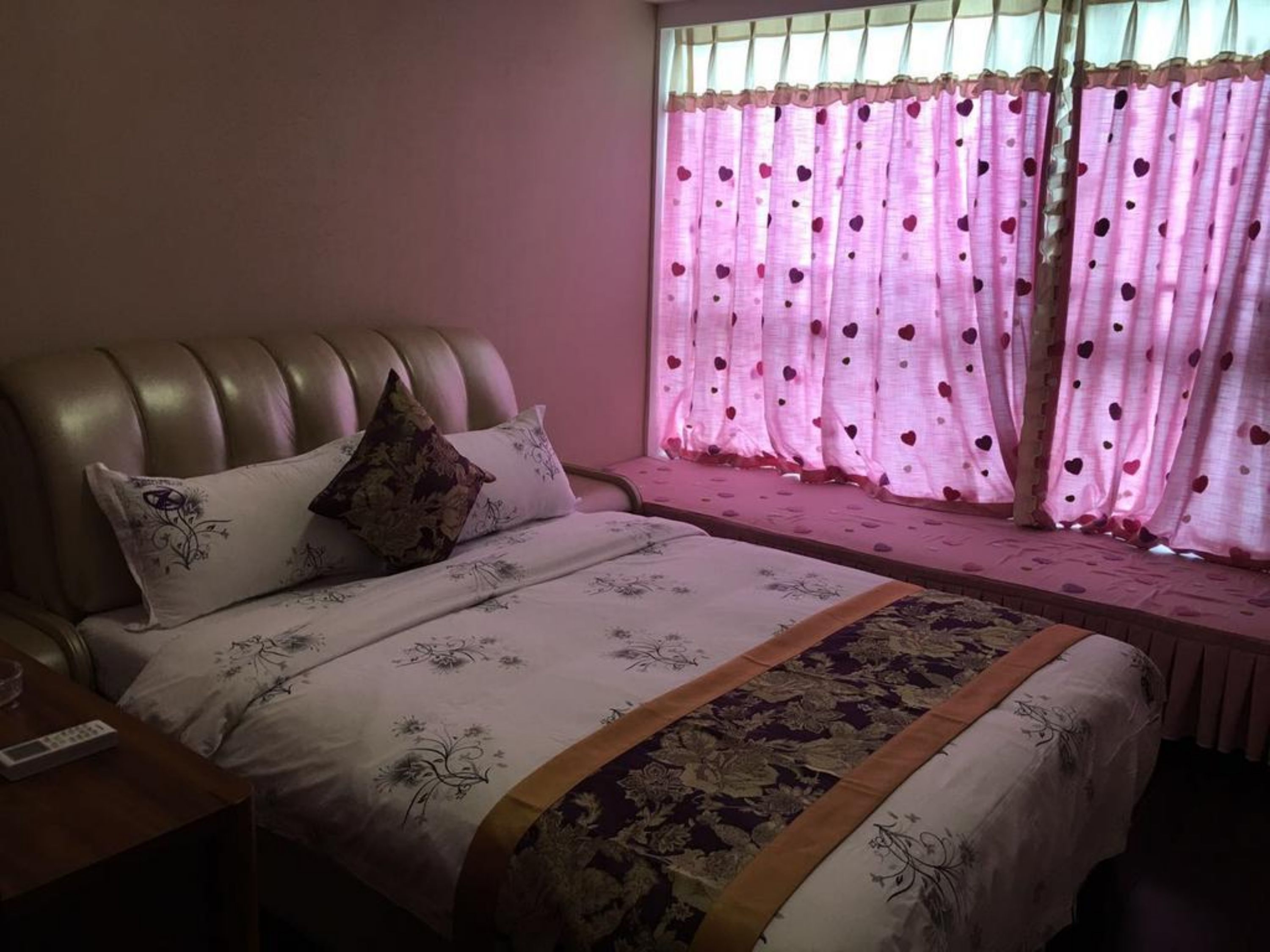 A bedroom with a bed, a nightstand, and a window with pink curtains.