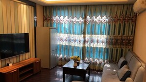 A living room with a flat-screen TV, wooden entertainment unit, sofa, and a dining table with a vase of flowers. - Zixinju Aparthotel (Changsha)