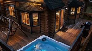 Una baita di legno con vasca idromassaggio, veranda in legno e numerose finestre.