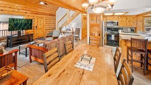 Interno di una baita di legno con zona pranzo, cucina e soggiorno.