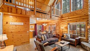A spacious log cabin with a 'WELCOME' sign, a dining area, and a cozy living room with multiple seating options.