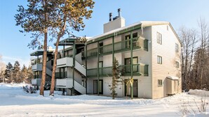 Ein mehrstöckiges Gebäude mit grüner Fassade und weißem Putz, das eine zentrale Treppe und mehrere Balkone aufweist.