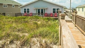Une maison située en bord de mer, dotée d’une terrasse en bois et de chaises rouges.