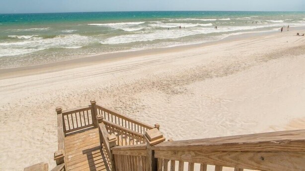 Un escalier en bois mène à une plage de sable, avec l’océan en toile de fond.