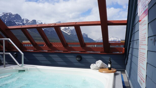 A hot tub with a mountain view, wooden deck, and a towel and bottle on the side.