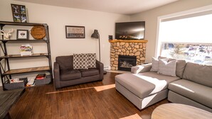 A living room with a stone fireplace, two sofas, a coffee table, and a TV mounted above the fireplace.