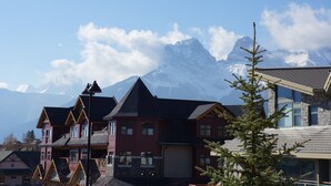 A chalet-style building with a steep roof, a balcony, and a mountain backdrop.