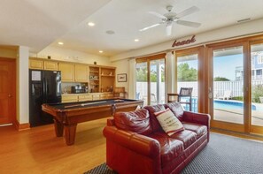A pool table in a room with a red leather couch and a ceiling fan. - Ocean-side 6BR Corolla escape with private pool, hot tub & game room BI-20 (Corolla)