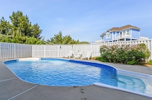 A swimming pool with a white fence, a house in the background, and trees around.
