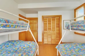 A room with two bunk beds, wooden flooring, and a wooden door in the background.
