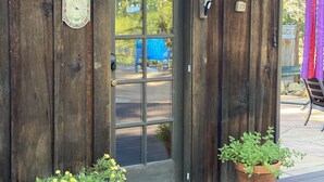 Un bâtiment en bois avec une porte en verre, une horloge et deux plantes en pot sur le porche.