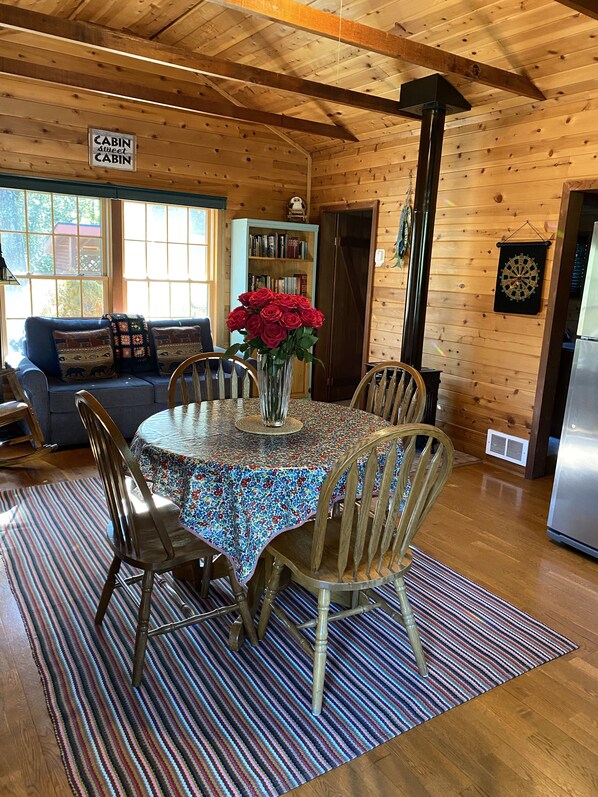 A cozy cabin interior with a dining table, chairs, a bookshelf, and a sign indicating the cabin's name. - Charming Riverside Retreat (Gasquet)