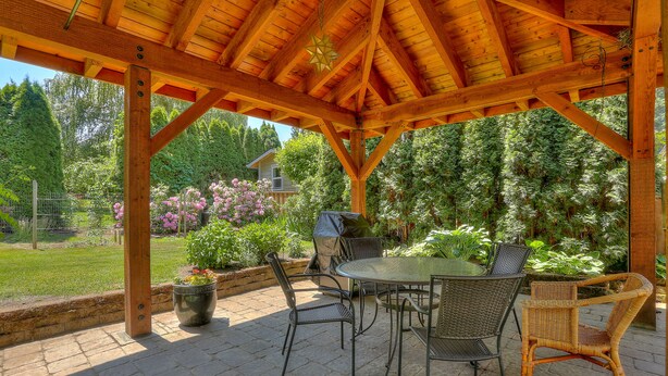 A covered patio with a wooden roof, outdoor furniture, and a view of a garden and house. - Living Color - Updated, Private Mid-Century in a Quiet, Convenient Neighborhood! (Hood River)