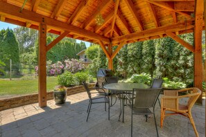 A covered patio with a wooden roof, outdoor furniture, and a view of a garden and house. - Living Color - Updated, Private Mid-Century in a Quiet, Convenient Neighborhood! (Hood River)