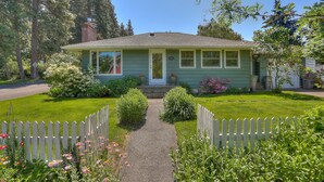 A green house with a front porch, a gravel path, and a white picket fence. - Living Color - Updated, Private Mid-Century in a Quiet, Convenient Neighborhood! (Hood River)
